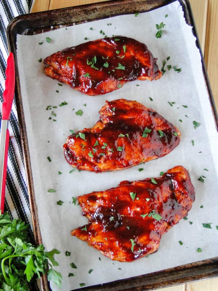 Top view of Oven roasted BBQ chicken breasts on sheet pan with tongs on the side of pan.