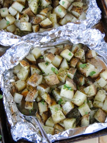 Grilled potatoes in foil packets opened and on sheet pan with serving spoon.