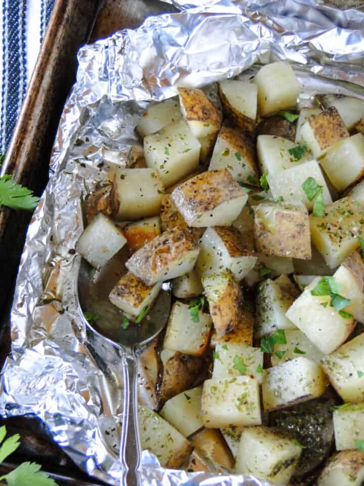 Grilled potatoes in foil with packet opened and spoon scooping potatoes.