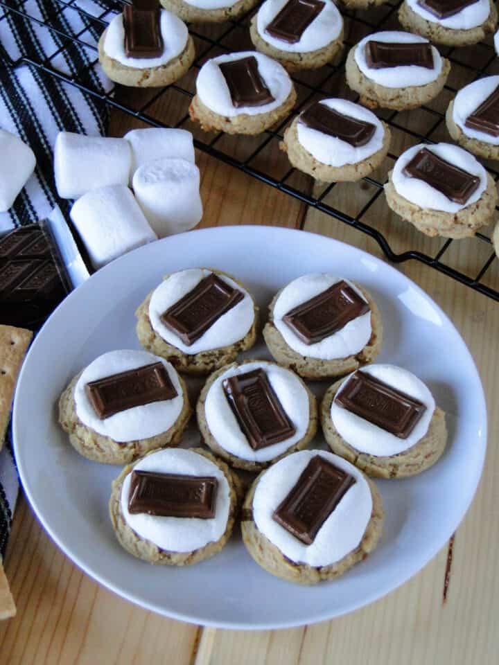 S'mores cookies on white round plate in front of wire rack of more cookies.