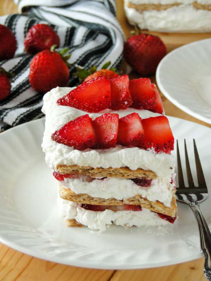 Close side view of Strawberry Shortcake Icebox Cake slice on white round plate with fork on the side.