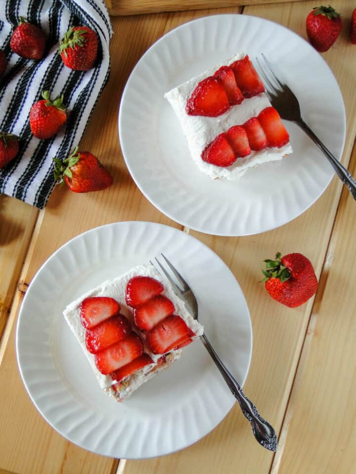Two slices of Strawberry Shortcake Icebox Cake on white round plates with forks.