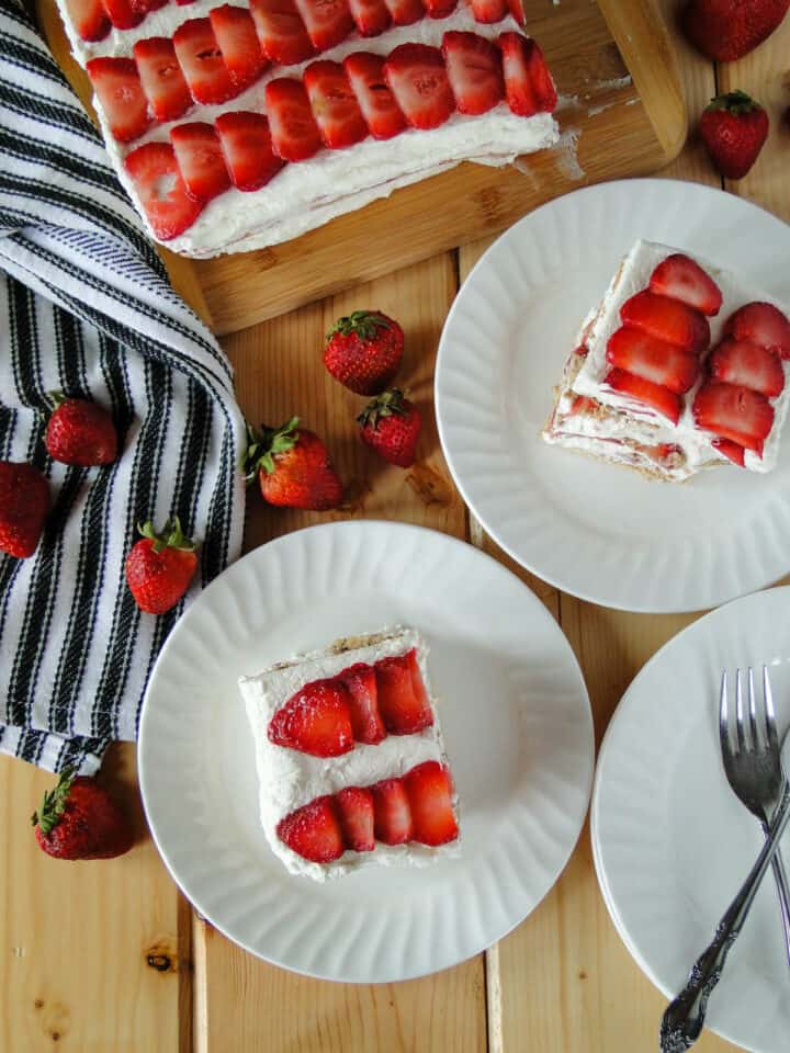 Strawberry Shortcake Icebox Cake slices on white round plates in front of whole cake.