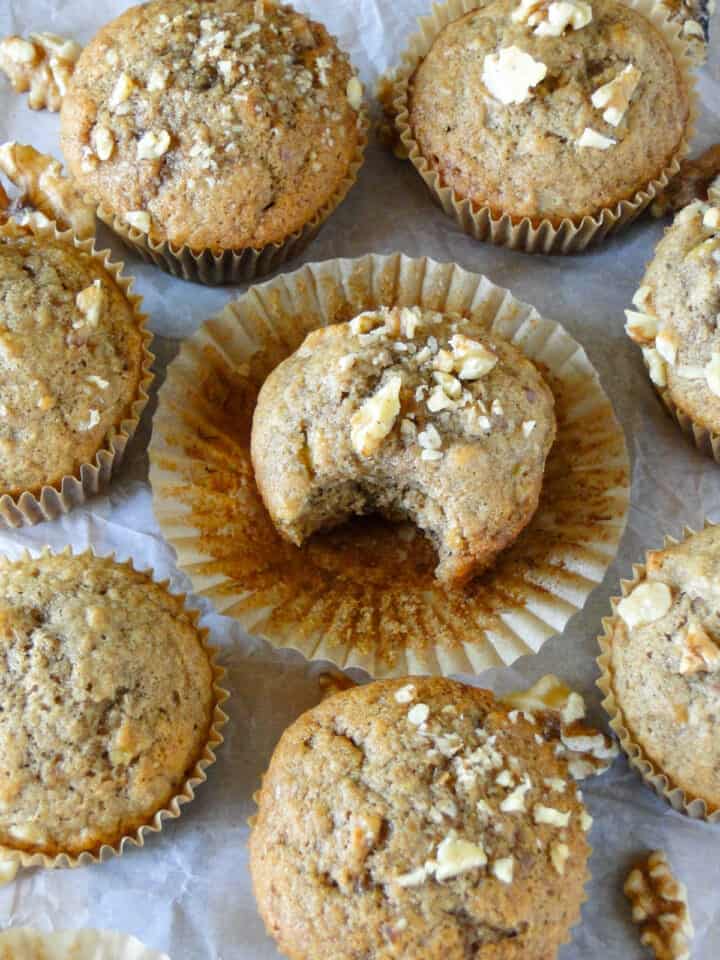 Banana nut muffin with wrapper peeled off and bite taken out it surrounded by more muffins.