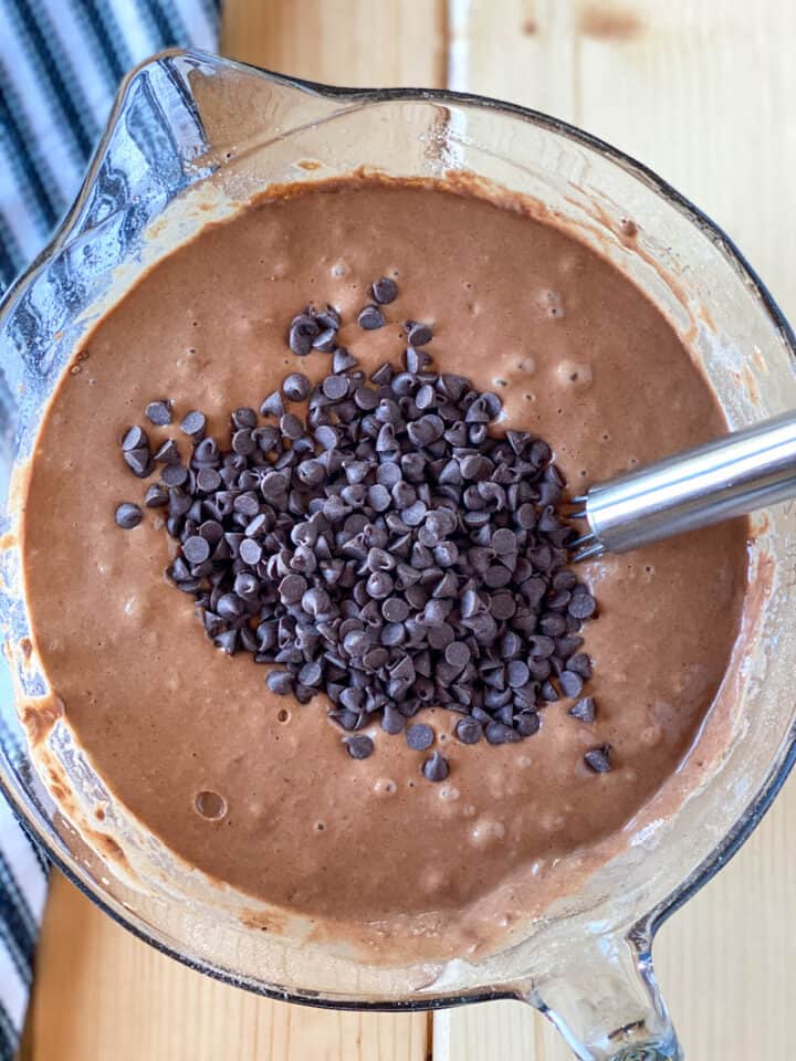 Waffle batter with chocolate chips added on top in large glass mixing bowl.