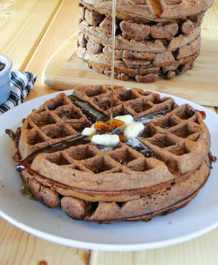 Chocolate waffles on white round plate with drizzle of maple syrup going on top.