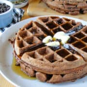 Side view of two chocolate waffles on white round plate with maple syrup on top.