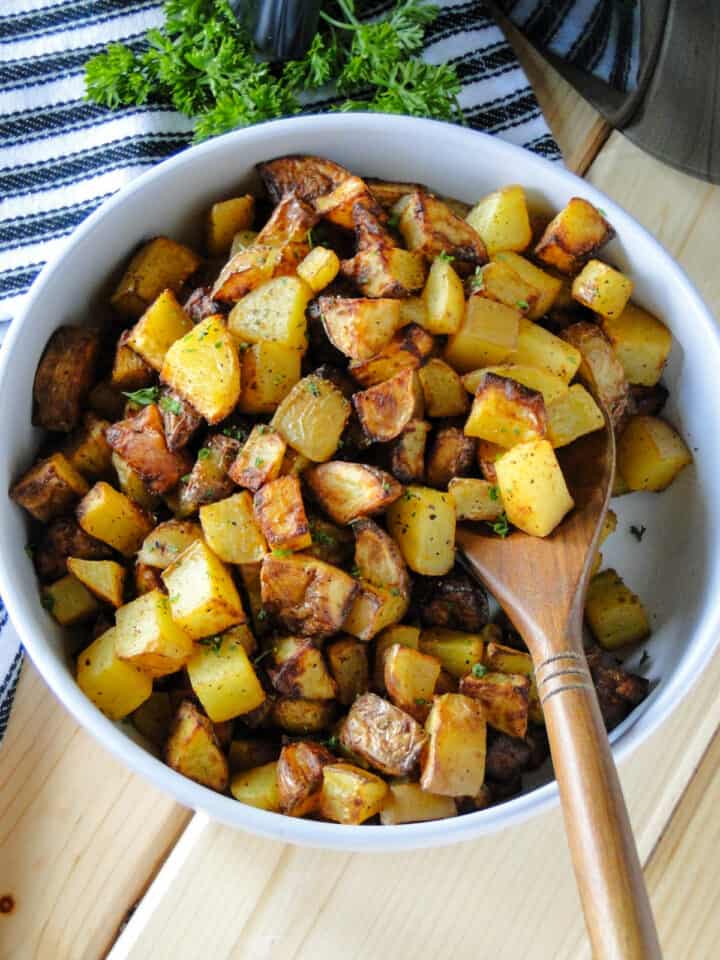 Air fryer potatoes in white round bowl with wood serving spoon scooping potatoes.