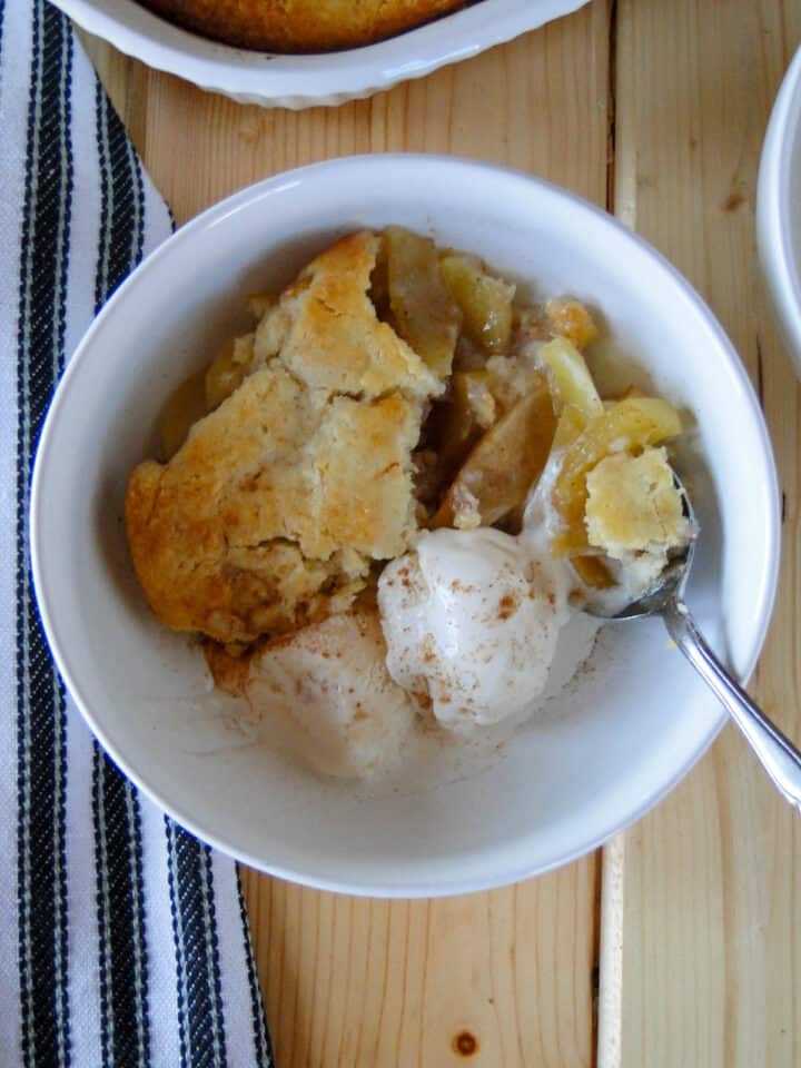 Top view of easy apple cobbler in white round bowl with bite on fork.