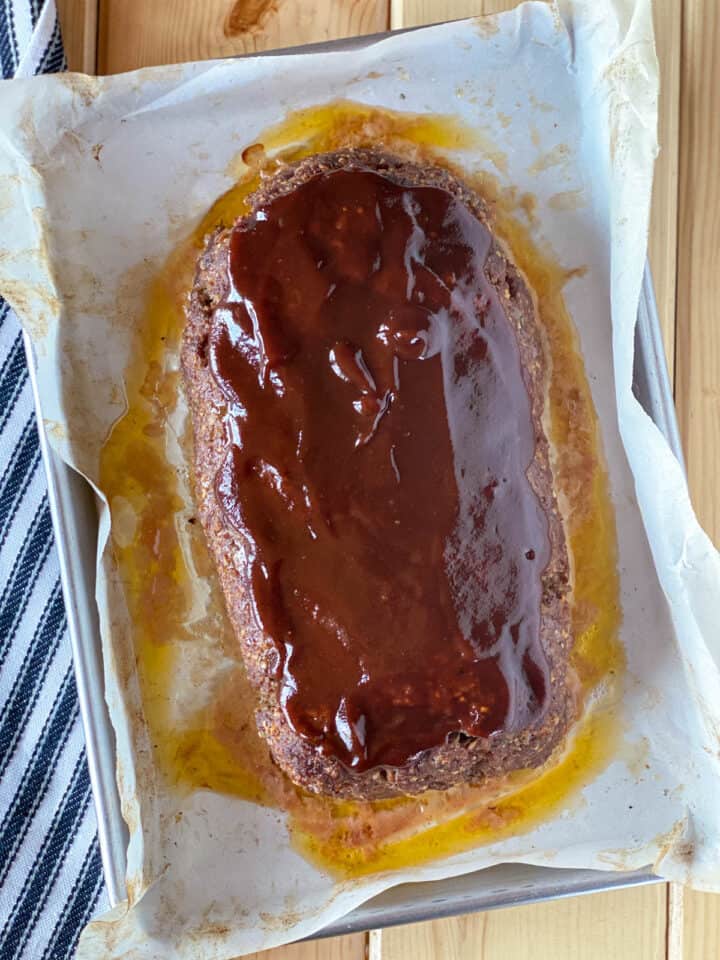 Half way cooked meatloaf on sheet pan with bbq sauce added to top.