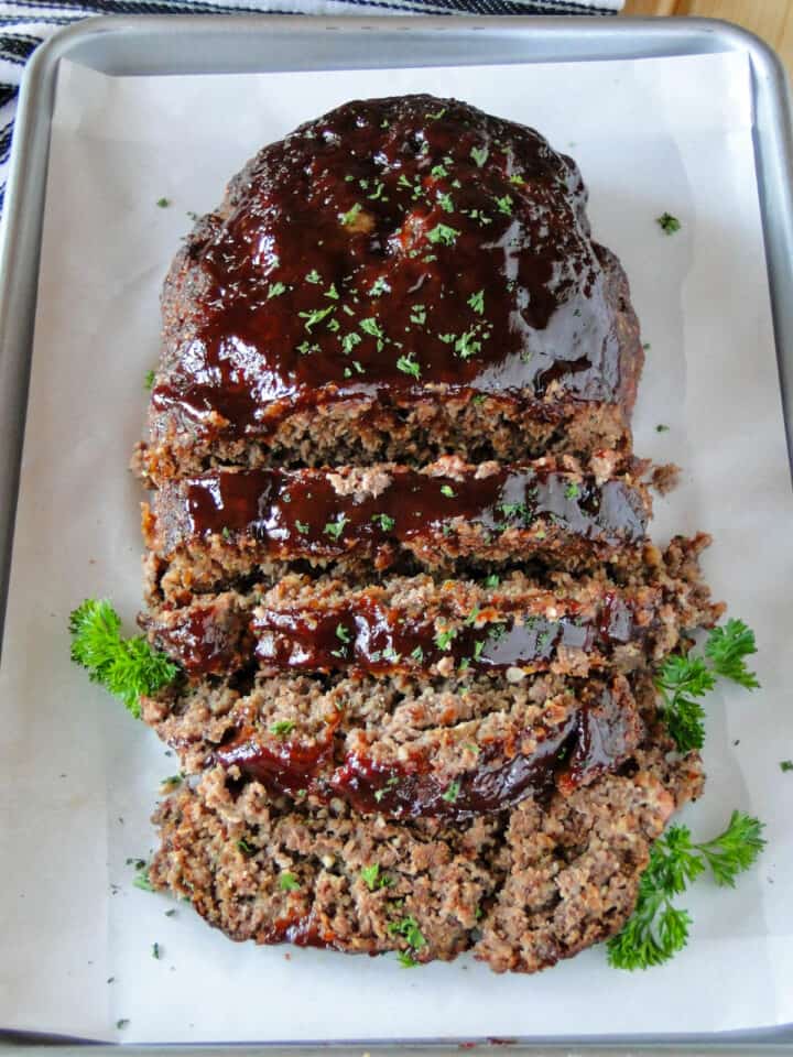 BBQ meatloaf on sheet pan sliced with parsley garnish.