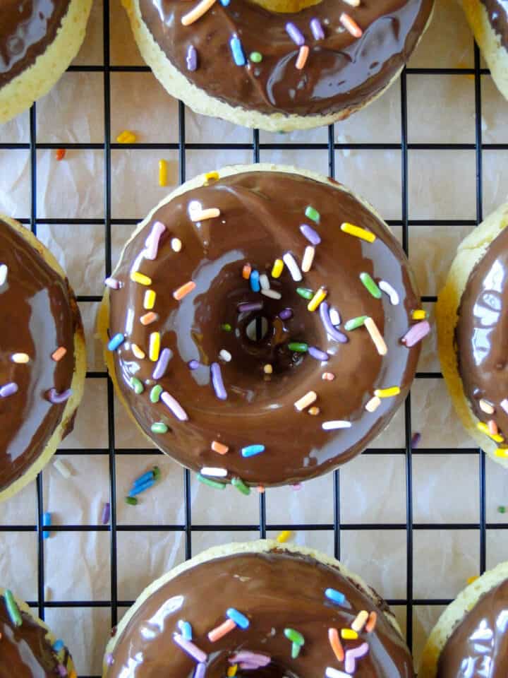 Top view of one baked cake donut with chocolate glaze and sprinkles on wire rack.