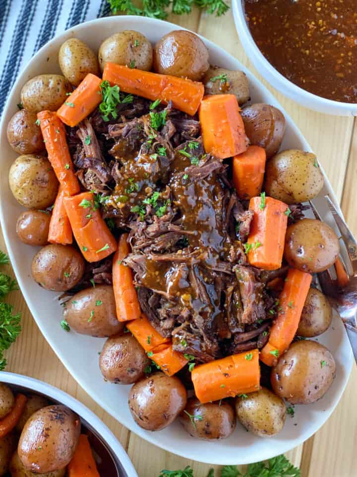 Instant Pot pot roast on oval serving plater with gravy over beef and serving fork on the side.