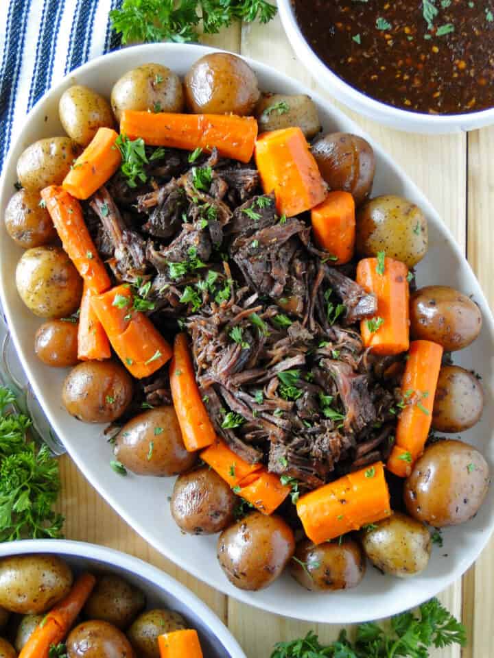 Closer view of Instant Pot pot roast on oval serving platter with extra potatoes and carrots in bowl next to platter and bowl of gravy on other side of platter.