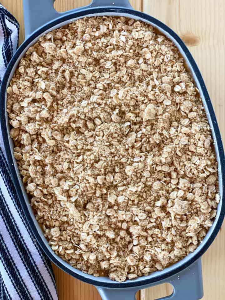 Oat topping sprinkled over filling in oval baking dish.
