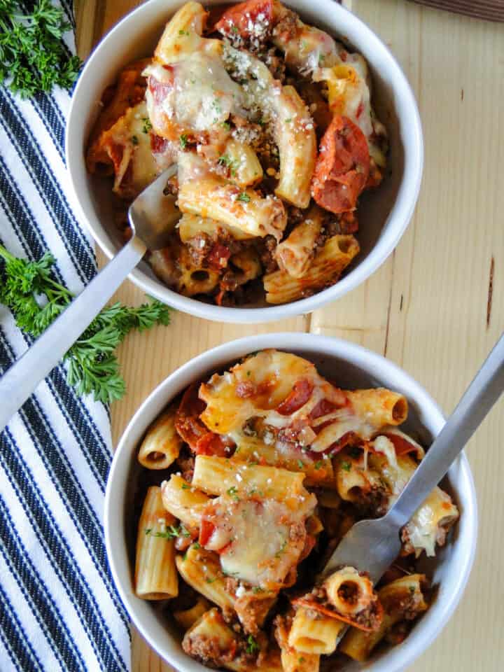 Two white round bowls with forks filled with pizza casserole.
