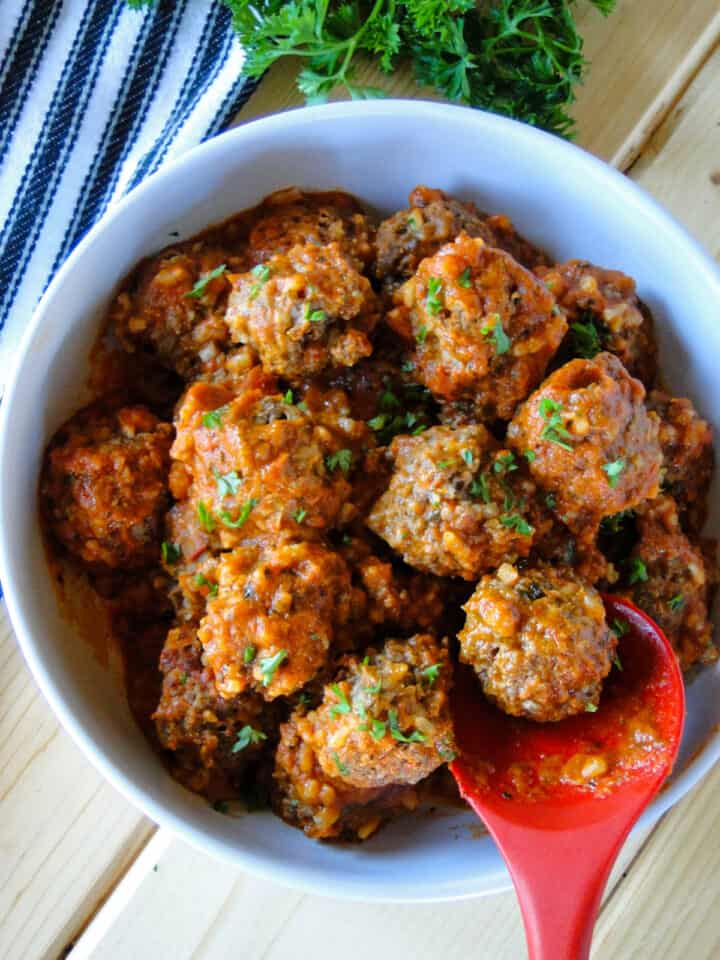 Instant pot porcupine meatballs in bowl with red serving spoon serving one meatball.