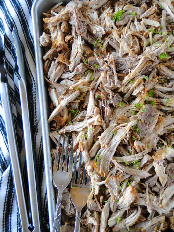 Pulled pork on sheet pan with two forks and tongs.