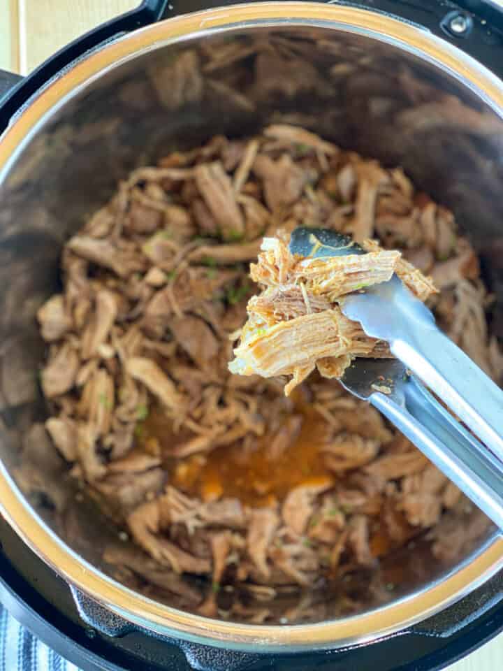 Pulled pork being served with tongs from instant pot.