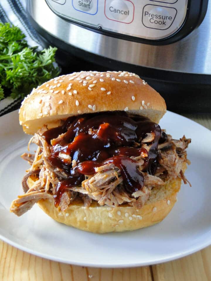 Close up view of pulled pork smothered in bbq suace on a sesame hamburger bun.