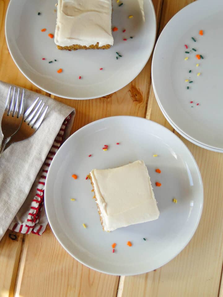 Pumpkin bars on white round plates with forks on napkin on side.