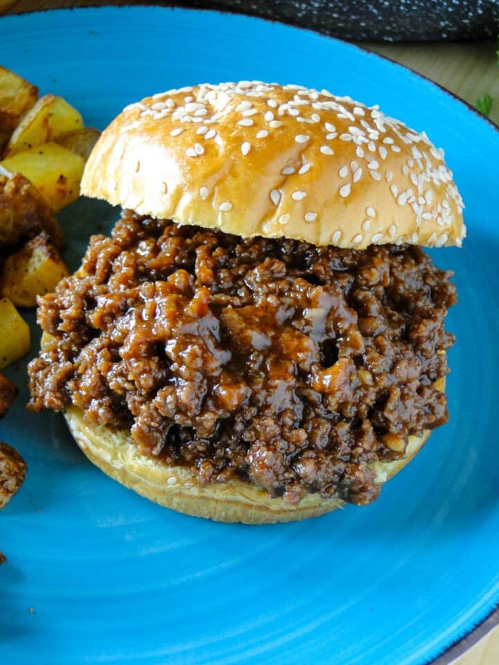 Close up top view of one easy homemade sloppy joe with top bun off to the side on blue plate.