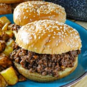 Side view of 2 easy homemade sloppy joes on blue plate in front of saucepan of sloppy joe mix and buns.