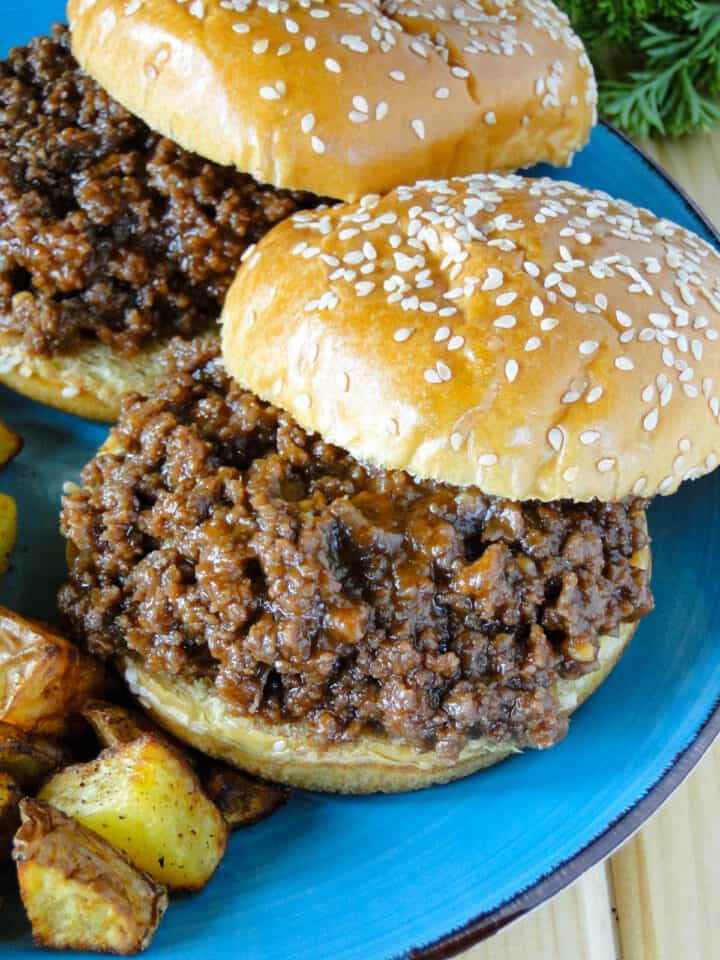 Two easy homemade sloppy joes with top buns off to the side on blue round plate.