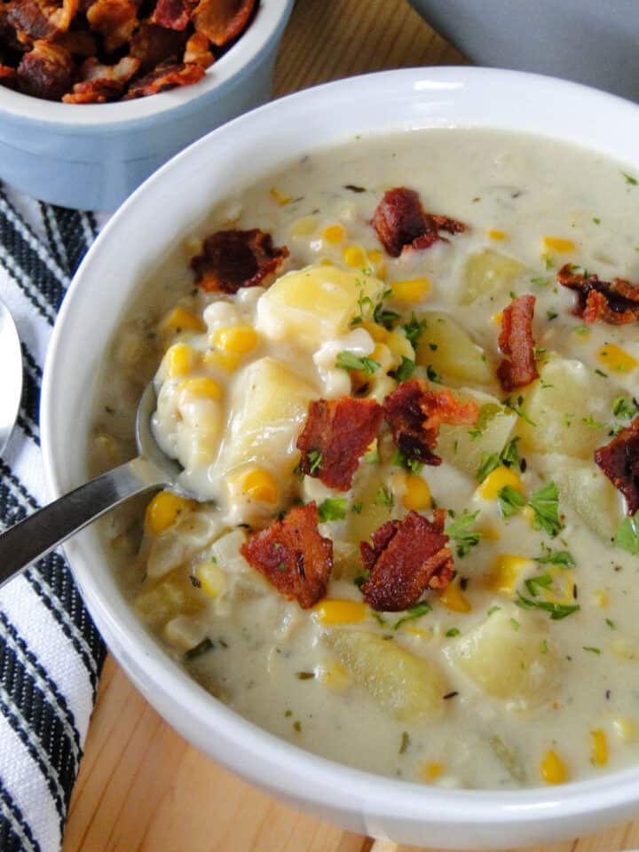 Creamy corn chowder with bacon pieces in white round bowl with bite on fork.