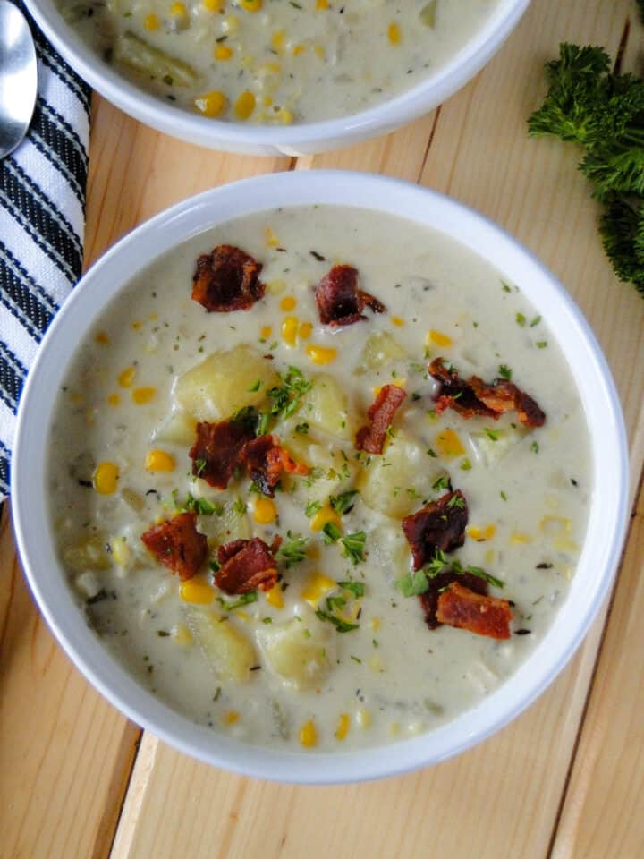 Top view of creamy corn chowder in white round bowl topped with bacon pieces.