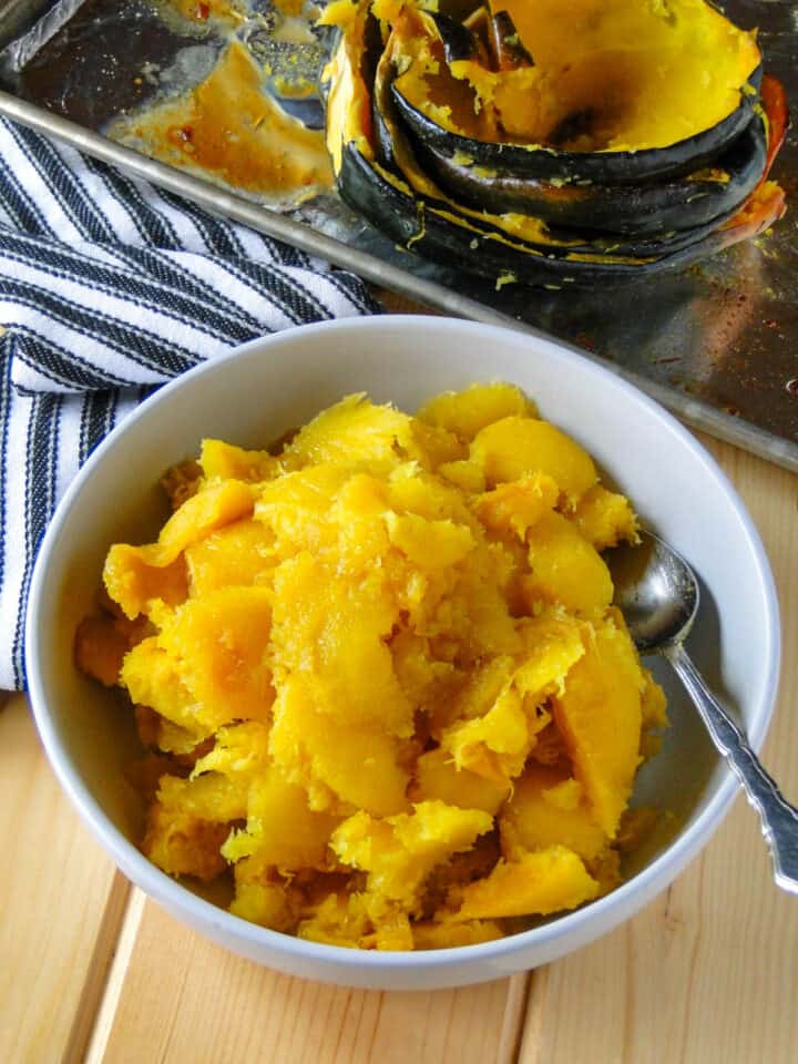Maple roasted acorn squash scooped out of skin and in serving bowl with spoon.