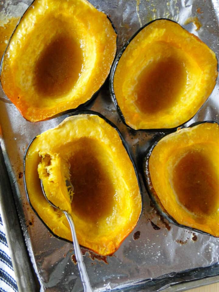 Maple roasted acorn squash halves on sheet pan with spoon in one half.