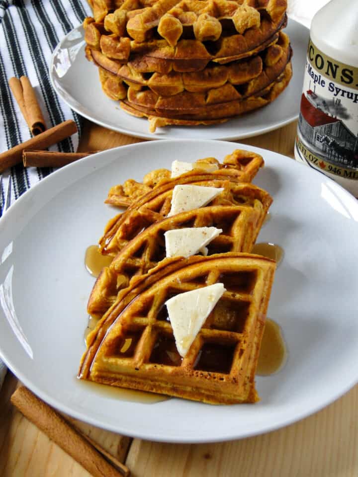 Quartered pumpkin waffle on white round plate in front of plate of more stacked waffles.