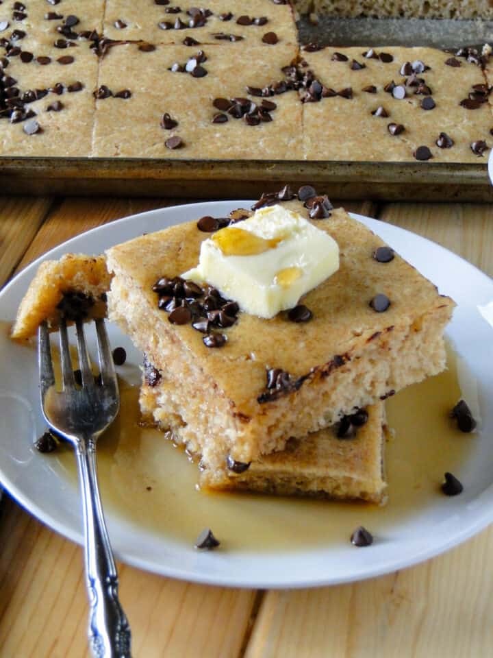 Two slices of sheet pan pancakes with chocolate chips on plate with bite on fork.
