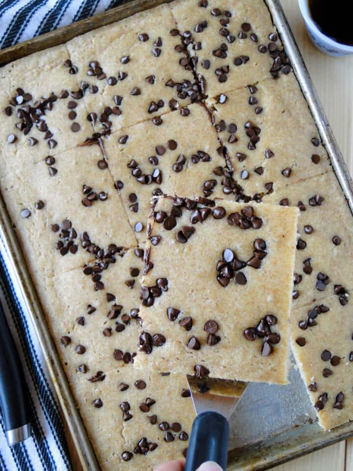 Sheet pan pancakes topped with mini chocolate chips in sheet pan with one slice on serving spatula.