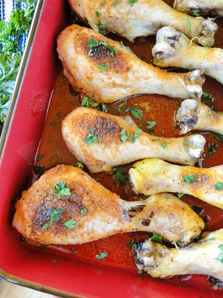 Close up of oven baked chicken legs in red baking dish.