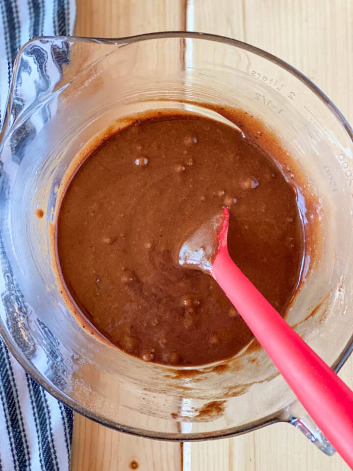 Brownie batter in glass mixing bowl with red spatula.