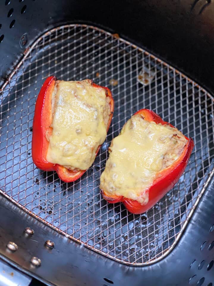 Sliced cheese added to stuffed peppers in air fryer basket.