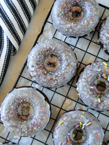 Chocolate sour cream baked donuts glazed with sprinkles on black wire rack.