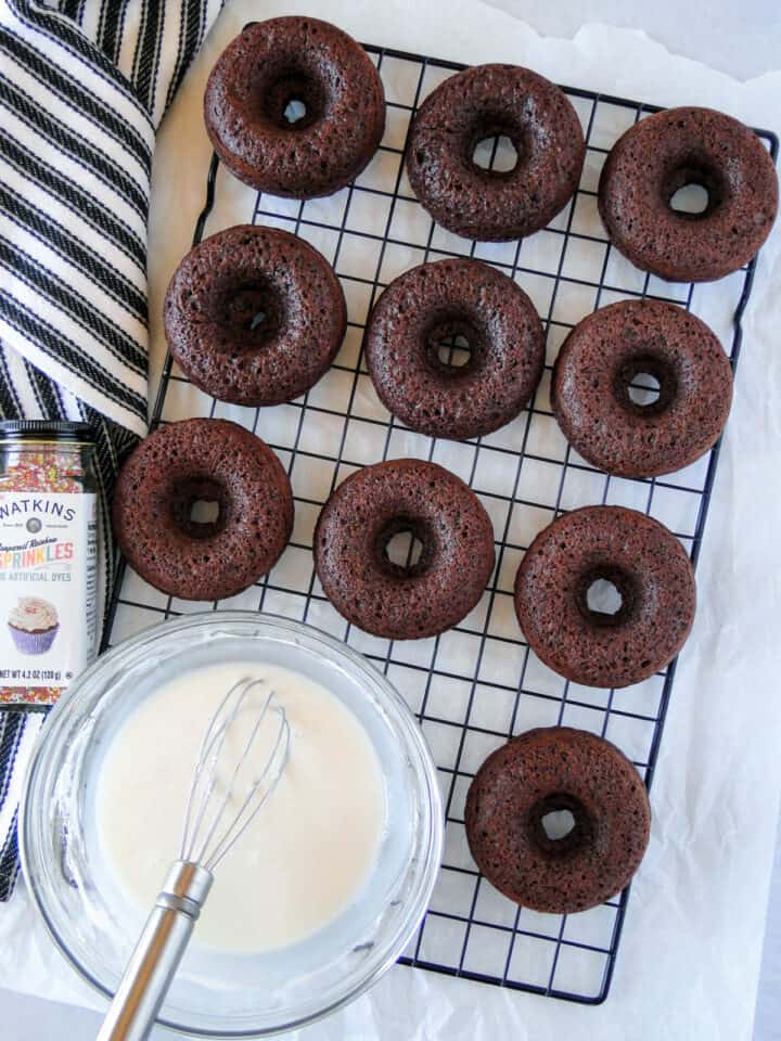 Chocolate sour cream donuts cooling on wire rack with bowl of glaze next to them.