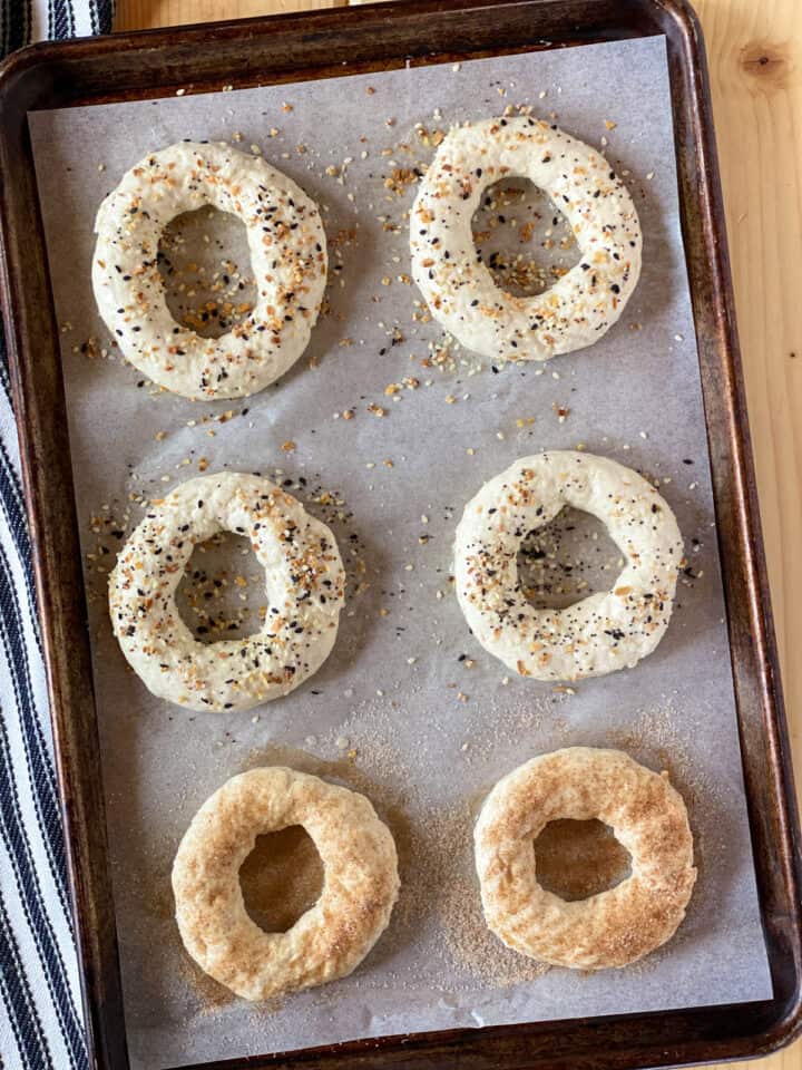 Bagels shaped and seasoned on parchment lined sheet pan.