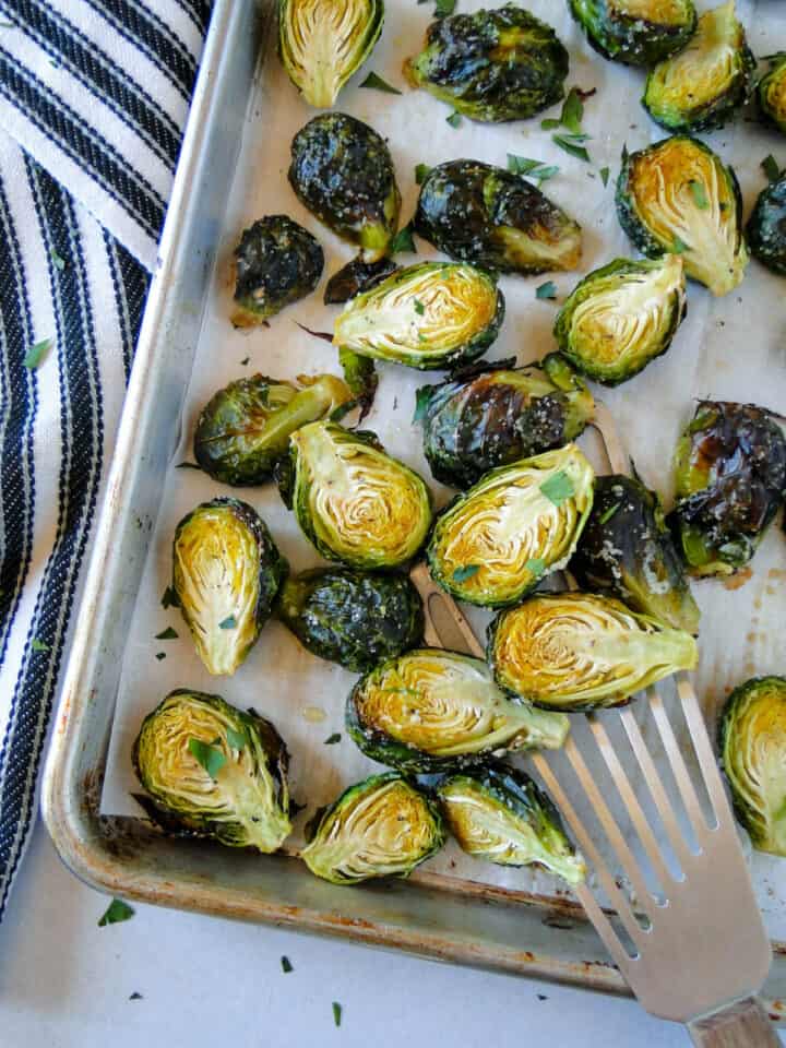 Close up view of roasted brussels sprouts on sheet pan with metal spatula.