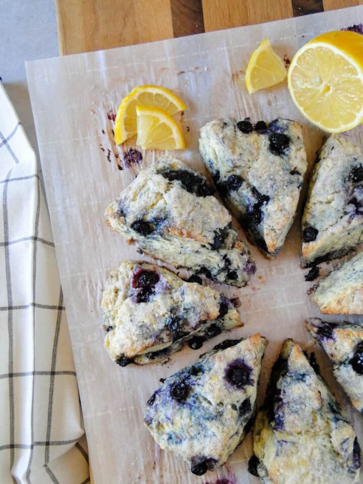 Blueberry scones in a circle with a lemon half and slices on the upper right side as garnish.