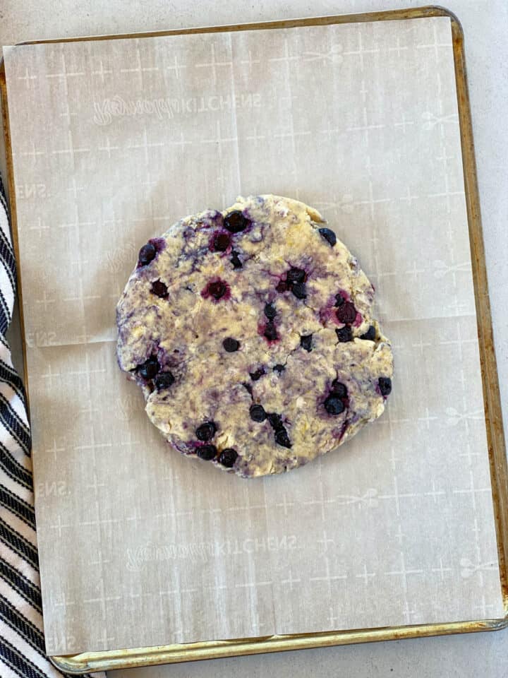 Scone dough patted into a circle on parchment lined baking sheet.