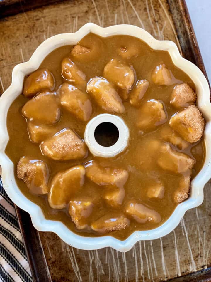 Caramel sauce poured over biscuit pieces in bundt pan on sheet pan.