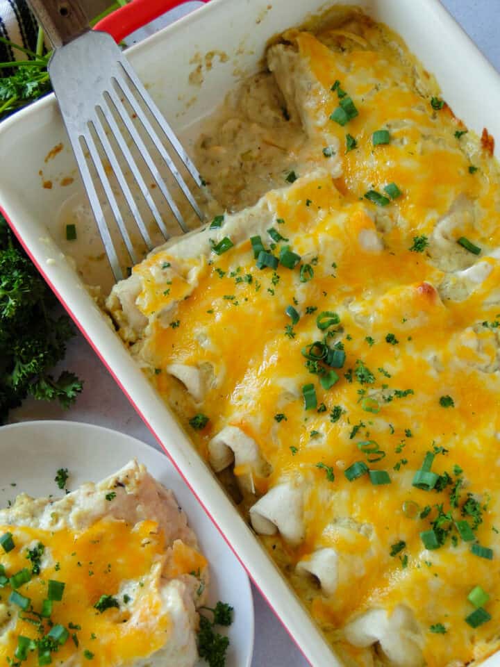 Salsa verde chicken enchiladas in baking dish with spatula and two enchiladas on white round plate.