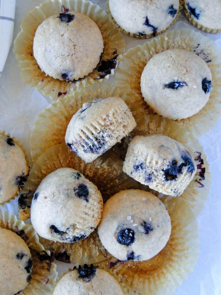 Top view of blueberry muffins in pile on top of paper liners and three muffins on their side.