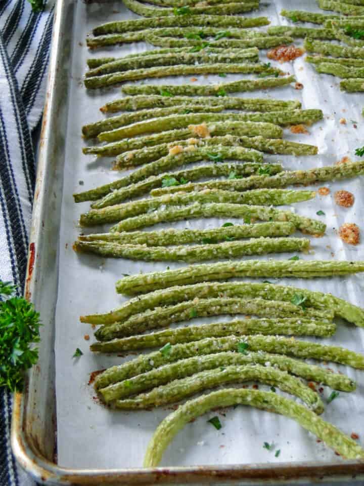Roasted garlic parmesan green beans in a neat row on baking sheet.