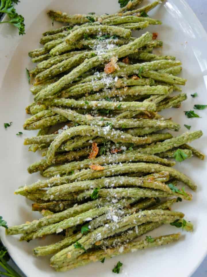 Garlic parmesan green beans on white oval plater with extra cheese for garnish.
