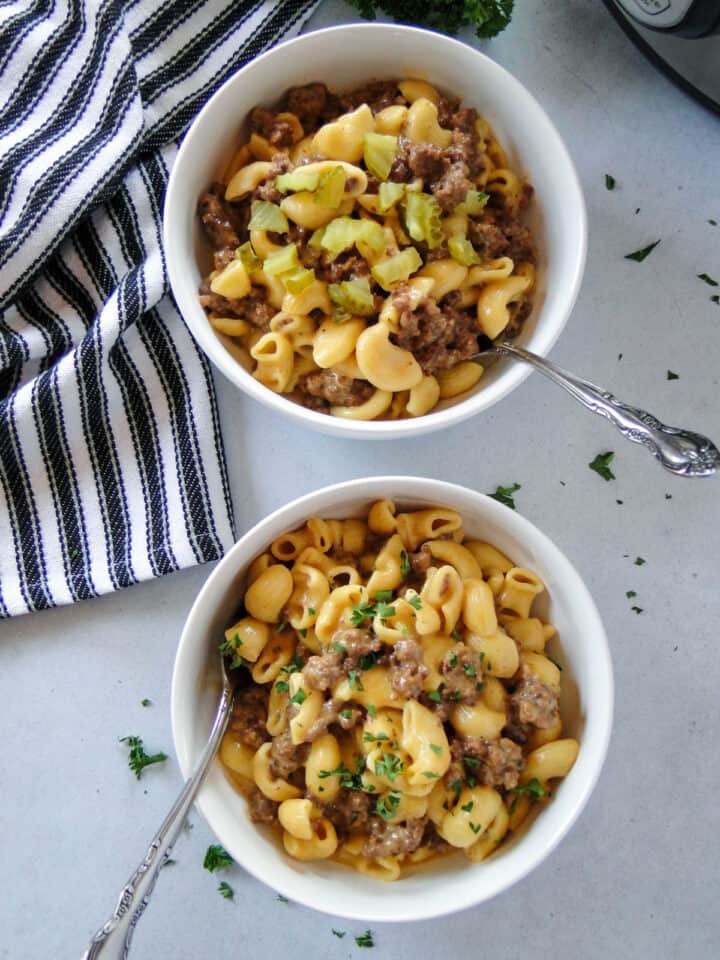 Instant pot cheeseburger macaroni in white bowls with forks and one bowl garnished with chopped pickles.